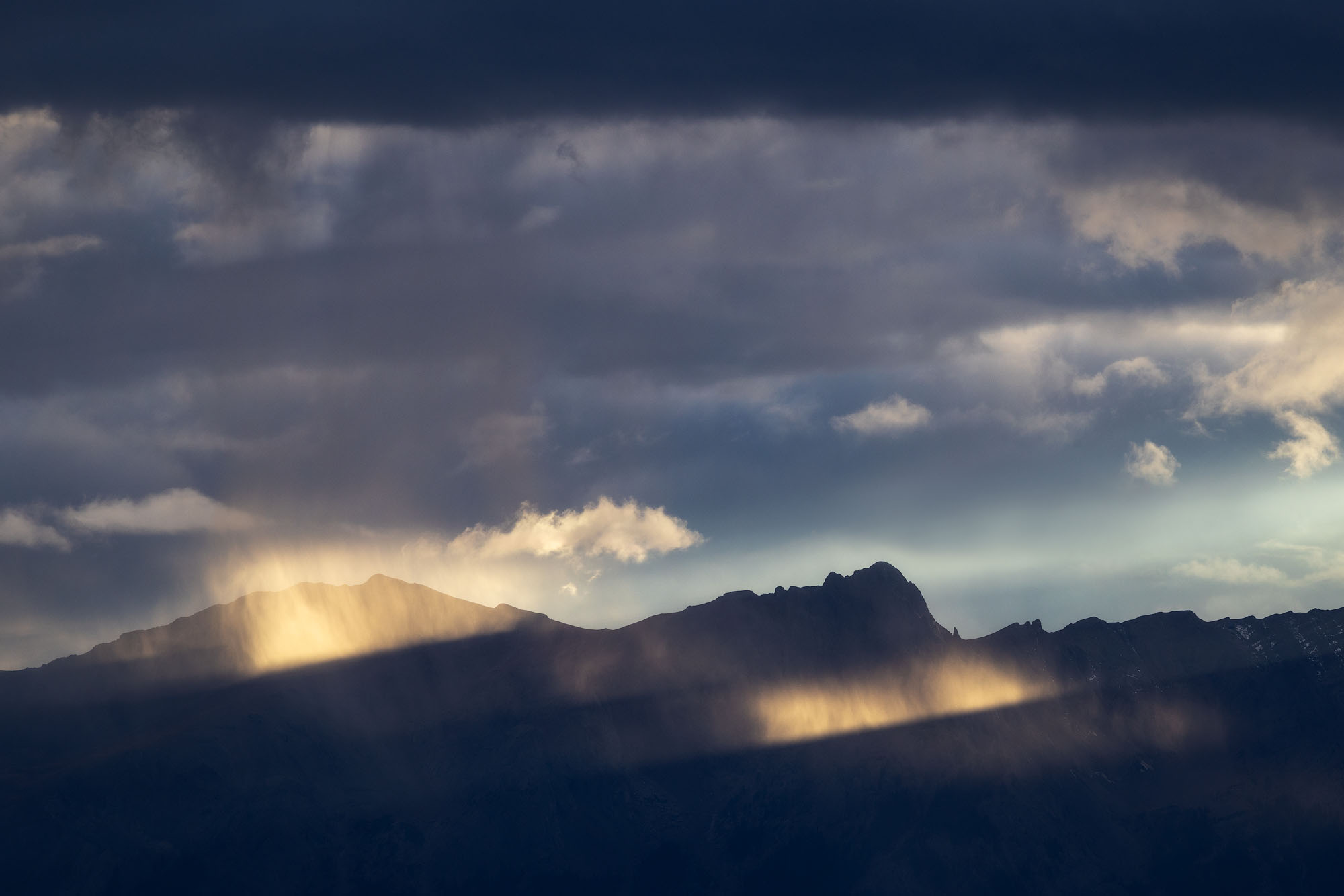 Late evening light shines through shafts of rain falling over the San Juan Mountains in southwestern Colorado.